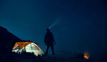 man standing beside camping tent wearing headlamp during nighttime
