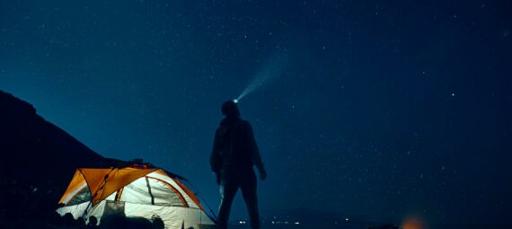 man standing beside camping tent wearing headlamp during nighttime